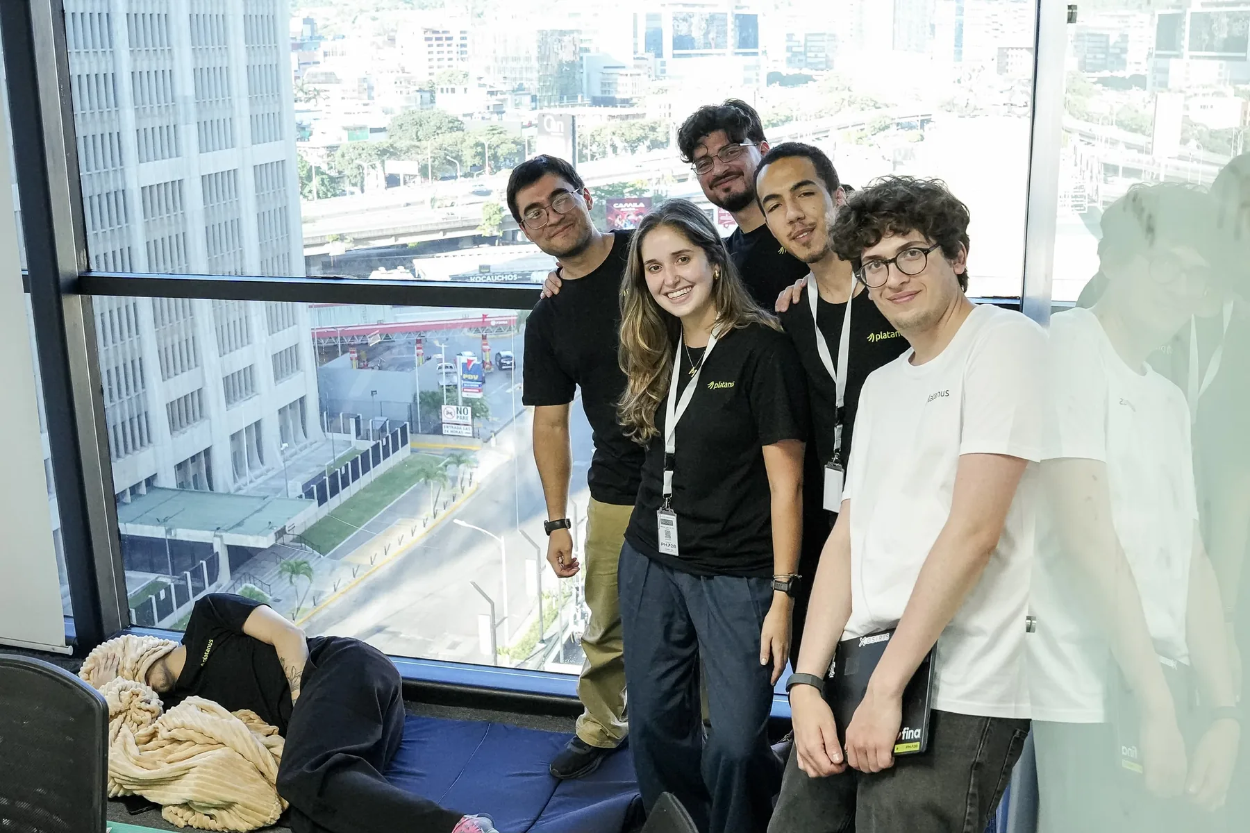 El equipo frente a la ventana con Caracas de fondo, y un compañero dormido en una colchoneta en el piso