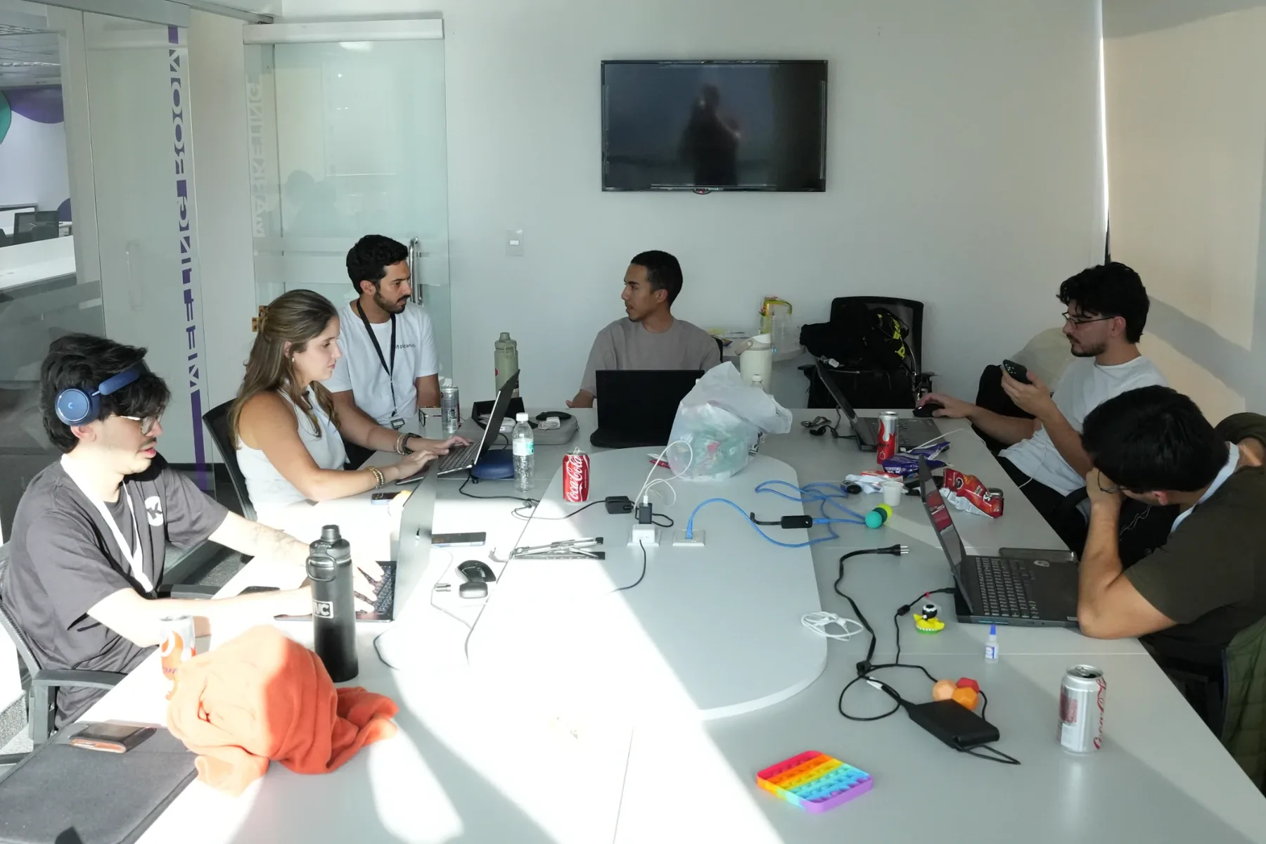 El equipo trabajando en sus laptops alrededor de una mesa con el mentor, entre latas de refresco y cables