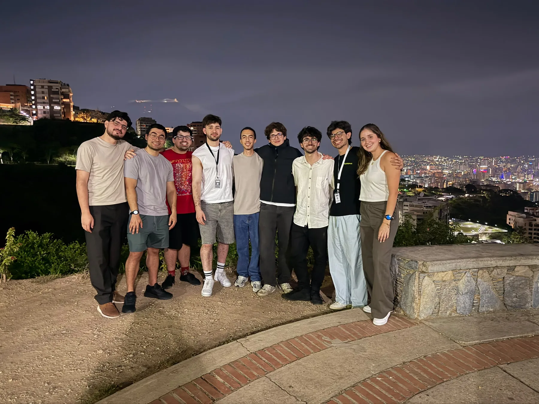 Nueve participantes del hackathon en un mirador de noche con las luces de Caracas detrás