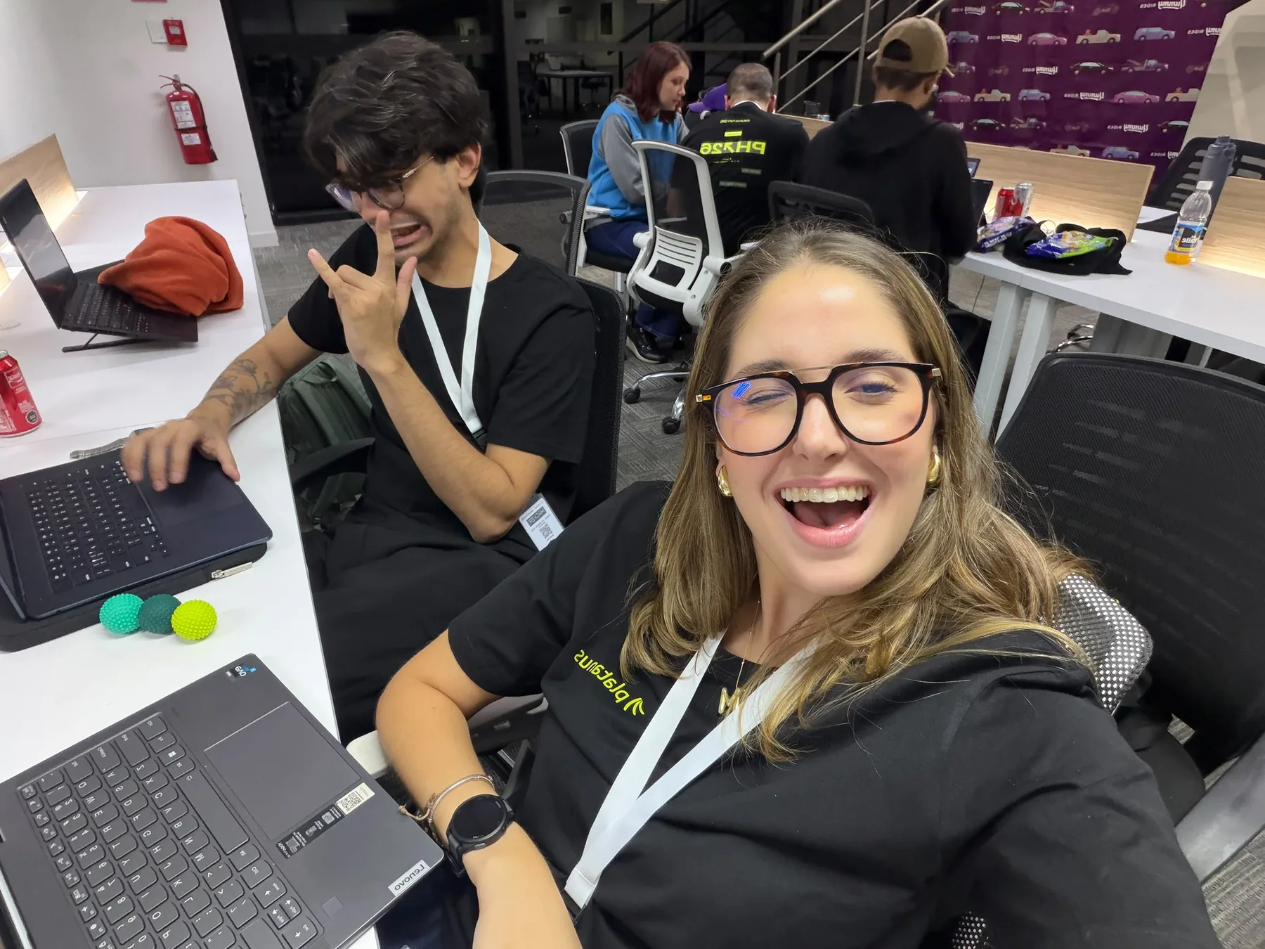 Selfie de Mariana riéndose con un compañero haciendo una mueca detrás, en el espacio del hackathon